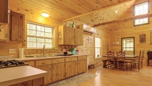 Ein Holzblockhaus-Interieur mit Küche, Essbereich und großen Fenstern.