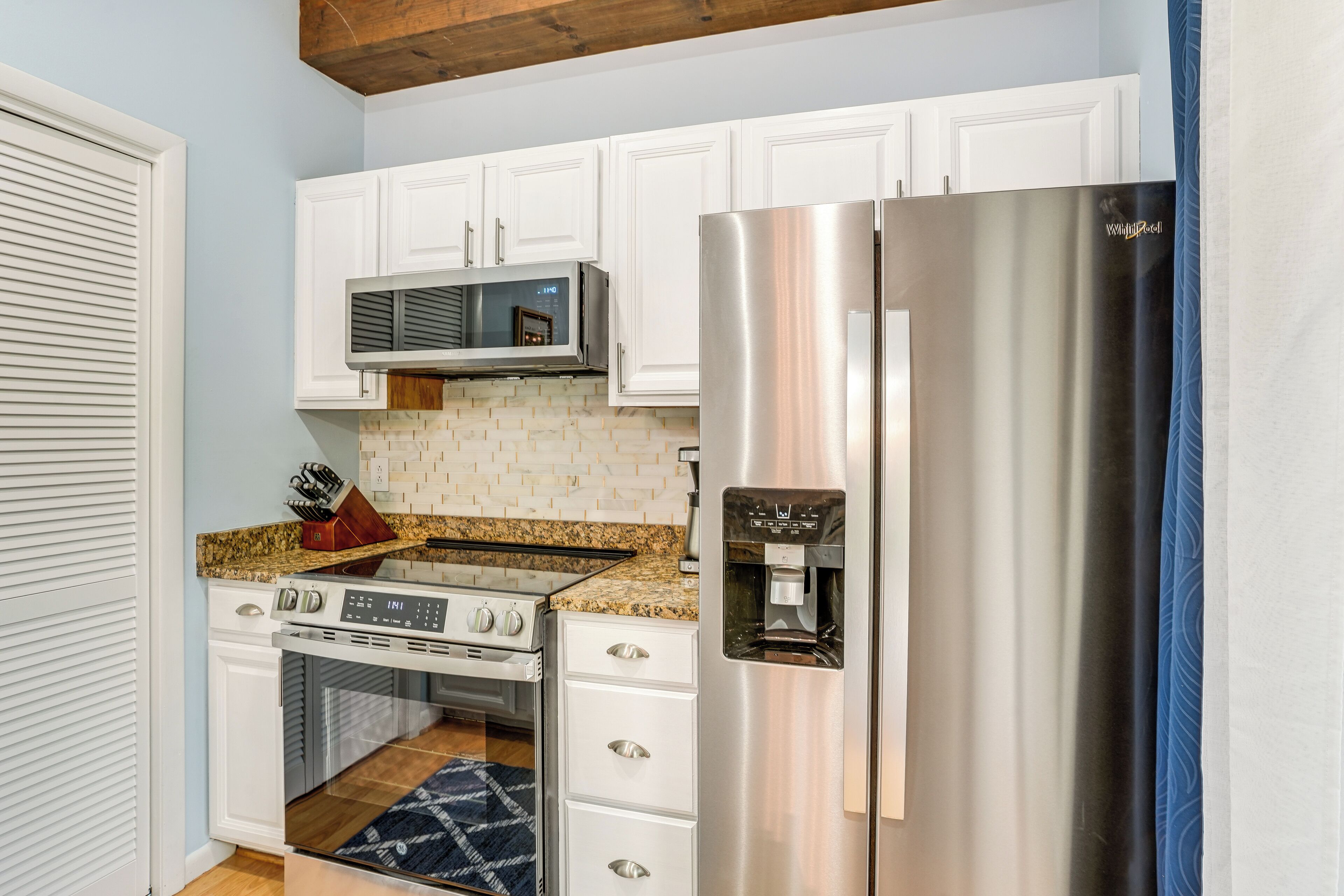 A kitchen with white cabinets, a stainless steel refrigerator, a microwave, and a built-in oven.