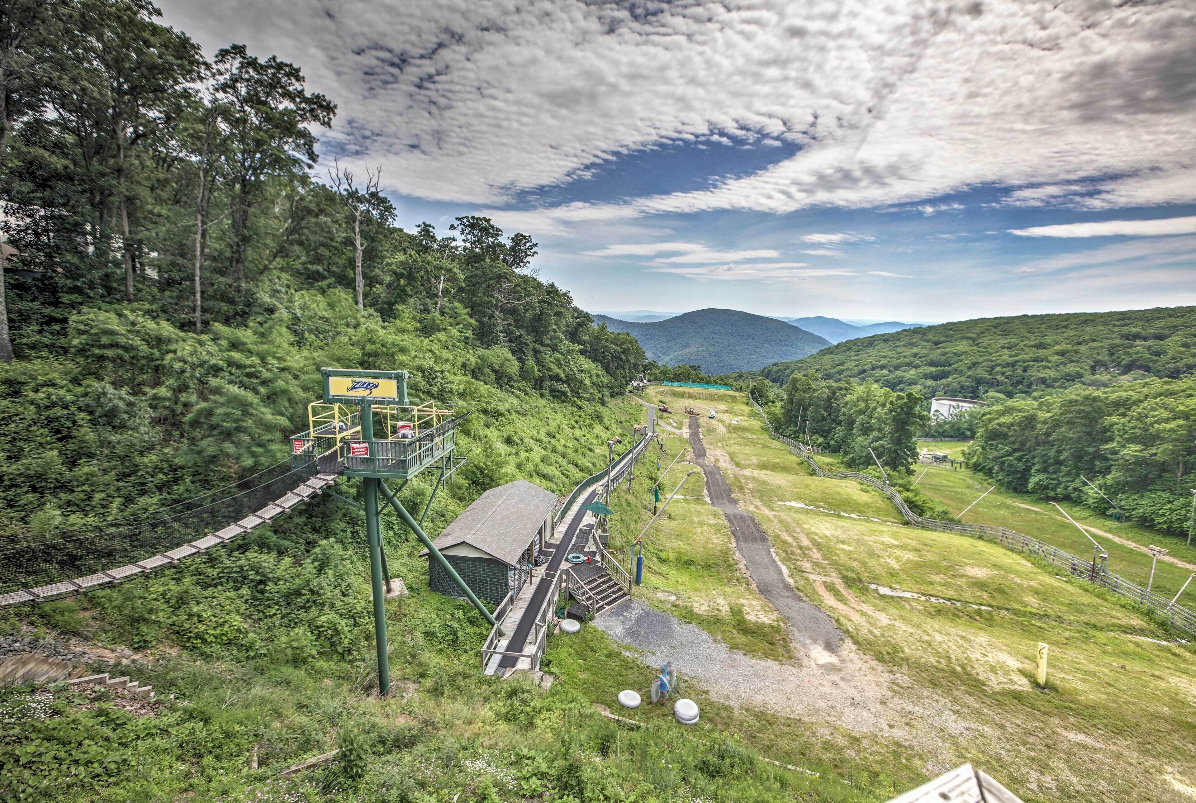 Un mirador panorámico con un puente colgante, un pequeño edificio y un camino que lleva a una zona verde distante.