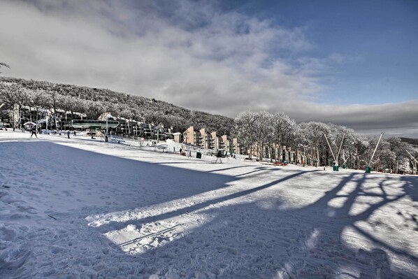 A snow-covered ski slope with buildings in the background and a clear sky. - Wintergreen Condo: Walk to Slopes,trails & Market! (Nellysford)