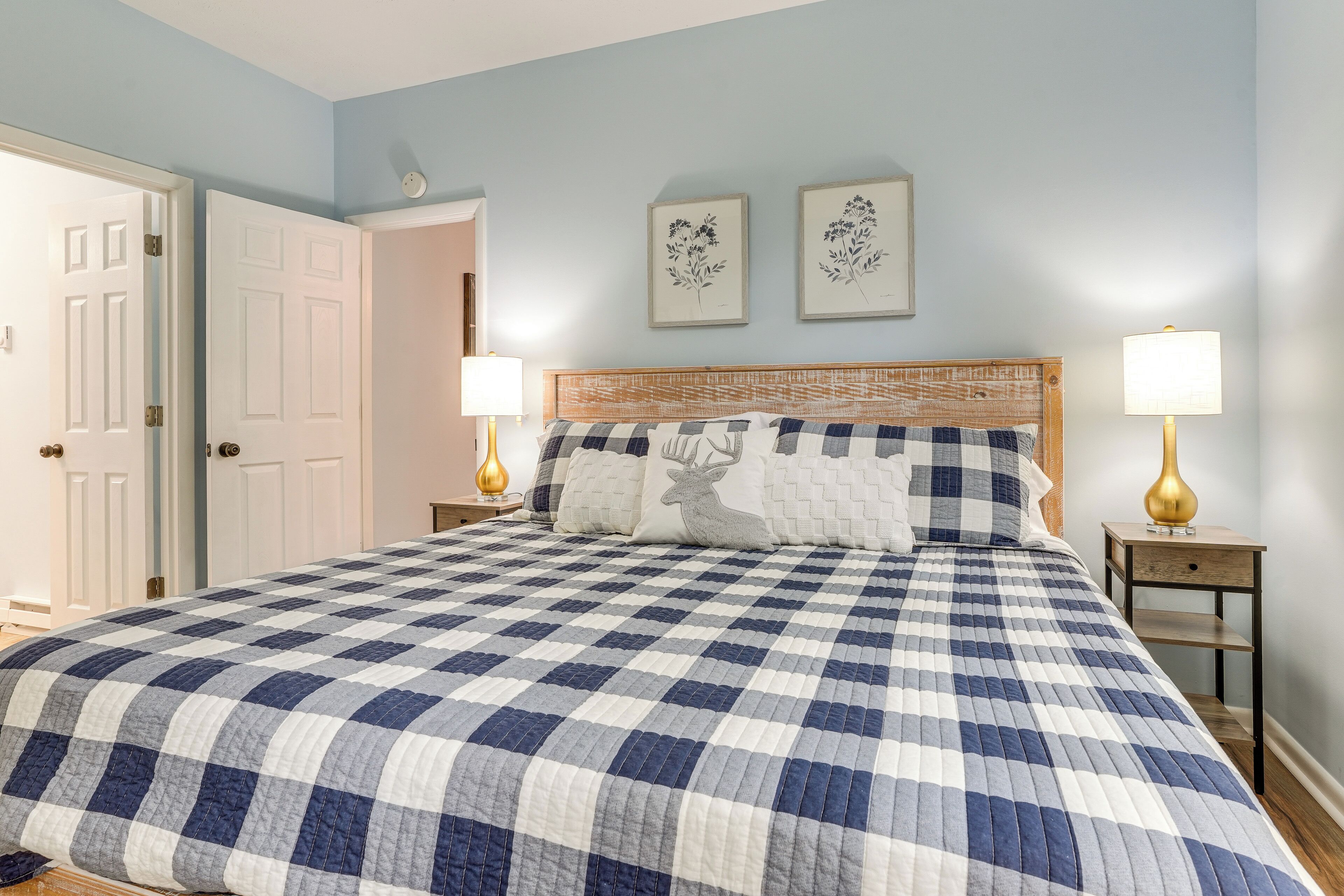A bedroom with a checkered bedspread, two wall-mounted picture frames, a wooden headboard, and two bedside lamps.