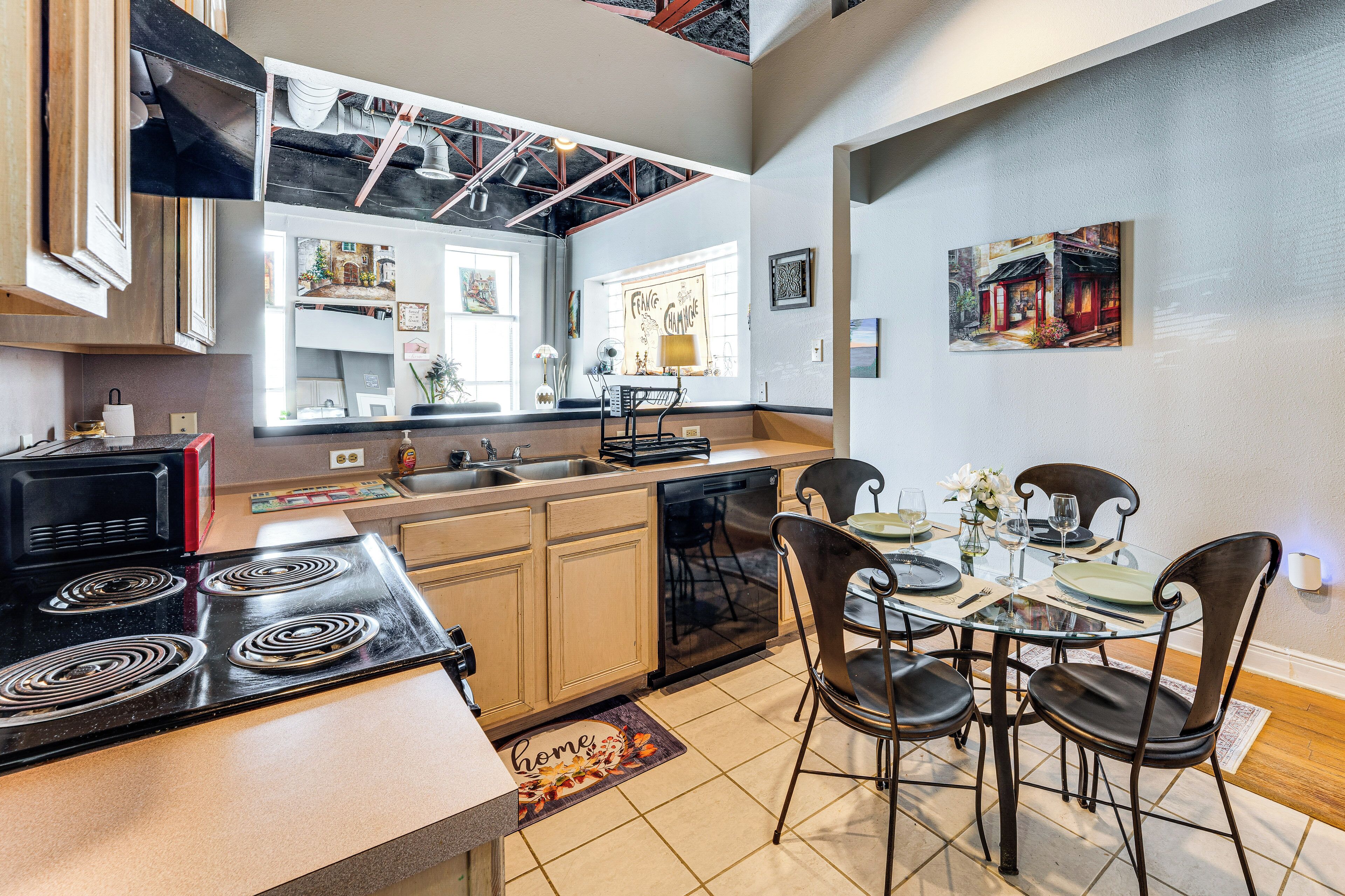 Uma cozinha moderna com ilha central, eletrodomésticos embutidos e área de jantar com mesa de vidro e cadeiras escuras.