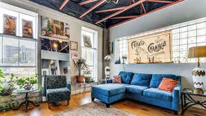 Ein Wohnzimmer mit einem blauen Sofa, einem gemusterten Teppich und einem großen Fenster mit Kunstwerken.