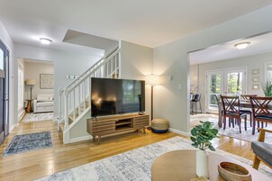 Una sala de estar moderna con un televisor de pantalla plana, un mueble de madera para entretenimiento y una escalera que sube a otro nivel.
