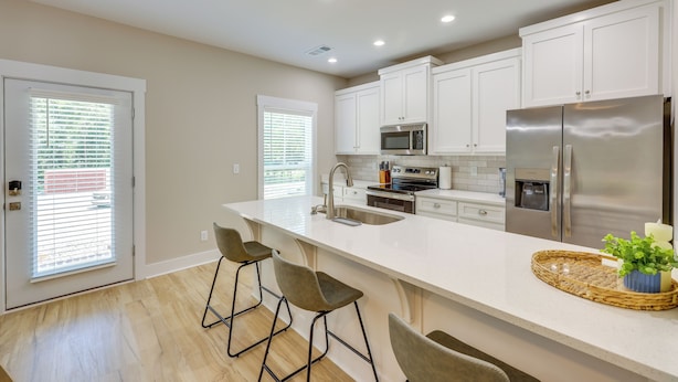 Una cocina moderna con armarios blancos, electrodomésticos de acero inoxidable y una isla grande con taburetes de bar.