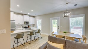 A modern kitchen with white cabinets, a microwave, and a stainless steel refrigerator. There is a dining area with a table and chairs, and a gray couch in the foreground. - Near 17 Springs Sports Complex: Millbrook Duplex! (Millbrook)