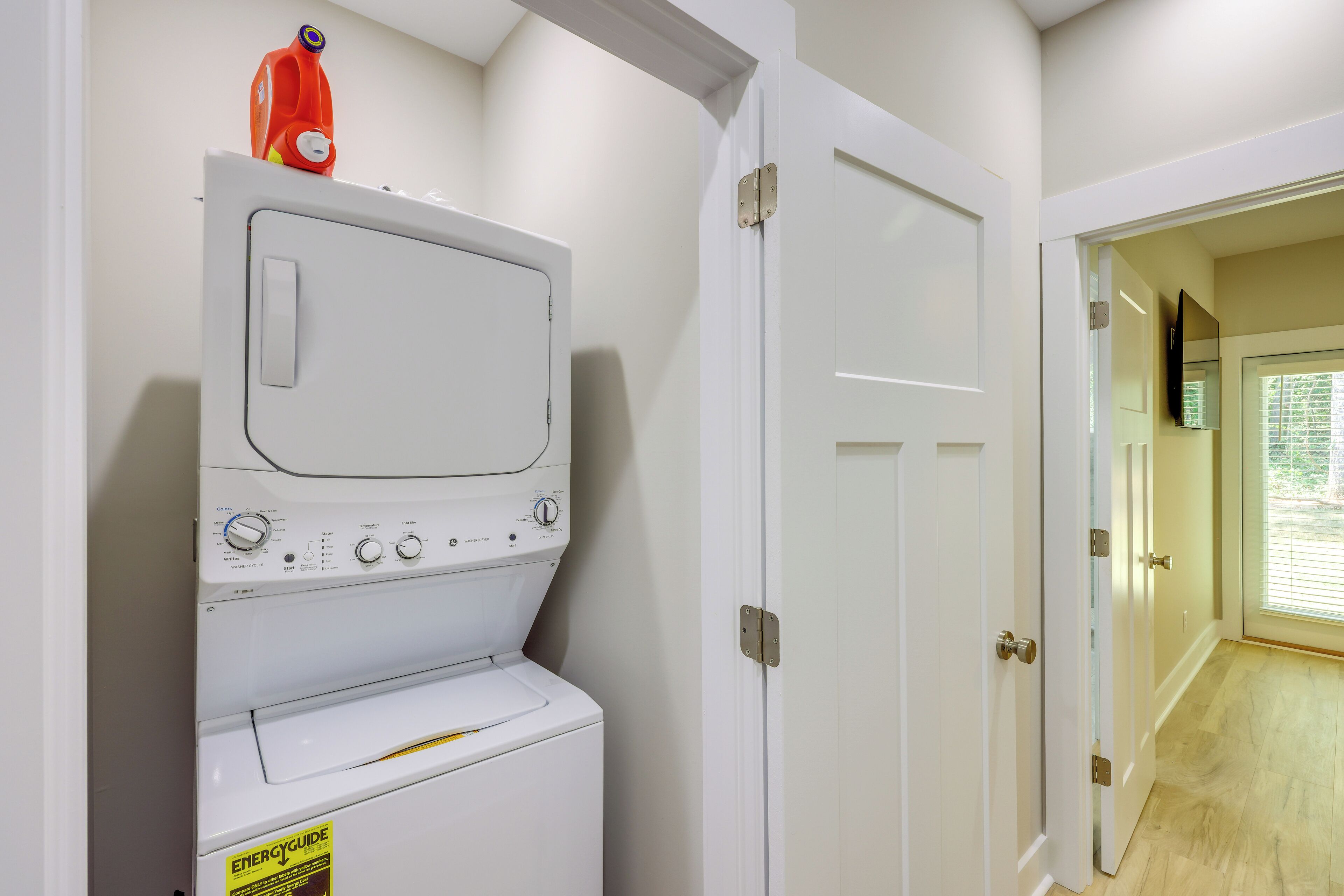 Un cuarto de lavado con lavadora y secadora de carga frontal, una puerta bisagra y vista a otra habitación a través de una puerta de vidrio.