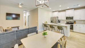 A modern kitchen with white cabinets, a central island with bar stools, a ceiling fan, recessed lighting, and a dining area with a gray sofa and a table. - Near 17 Springs Sports Complex: Millbrook Duplex! (Millbrook)