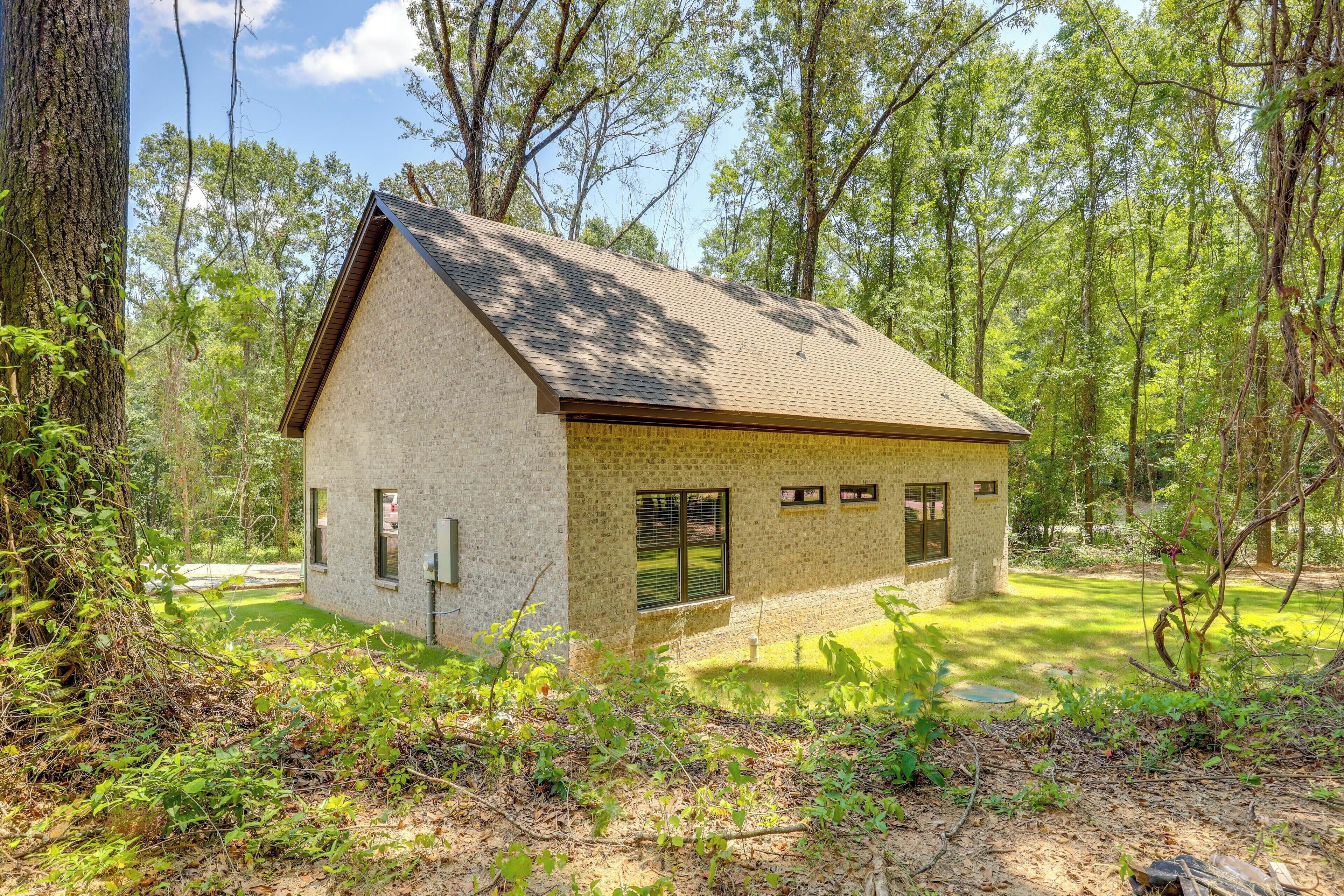 A small, single-story house with a sloped roof, surrounded by dense forest.