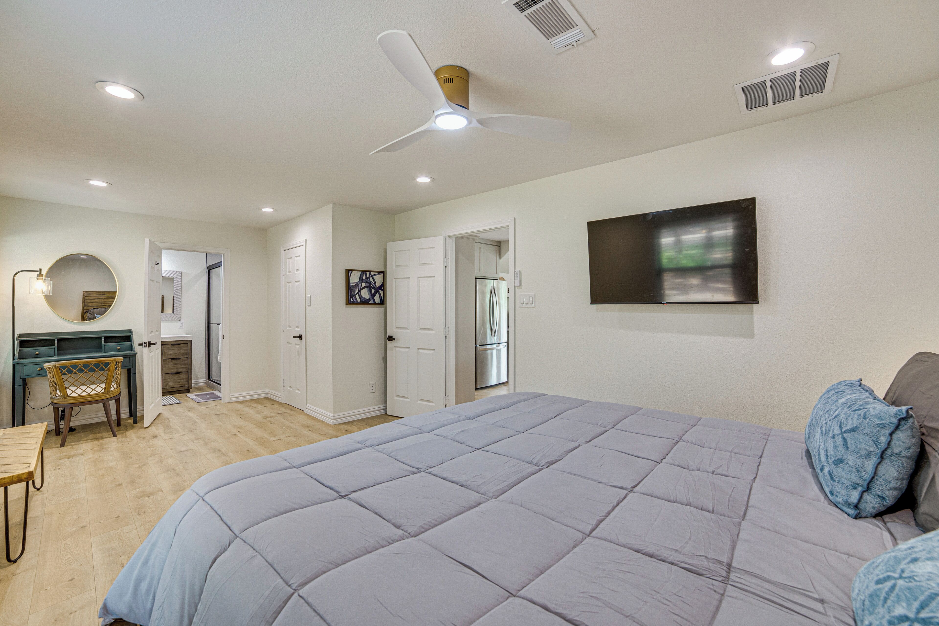 A bedroom with a large bed, a desk, and a chair. There is a ceiling fan and recessed lighting.