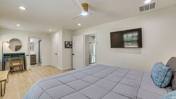 A bedroom with a large bed, a desk, and a chair. There is a ceiling fan and recessed lighting.