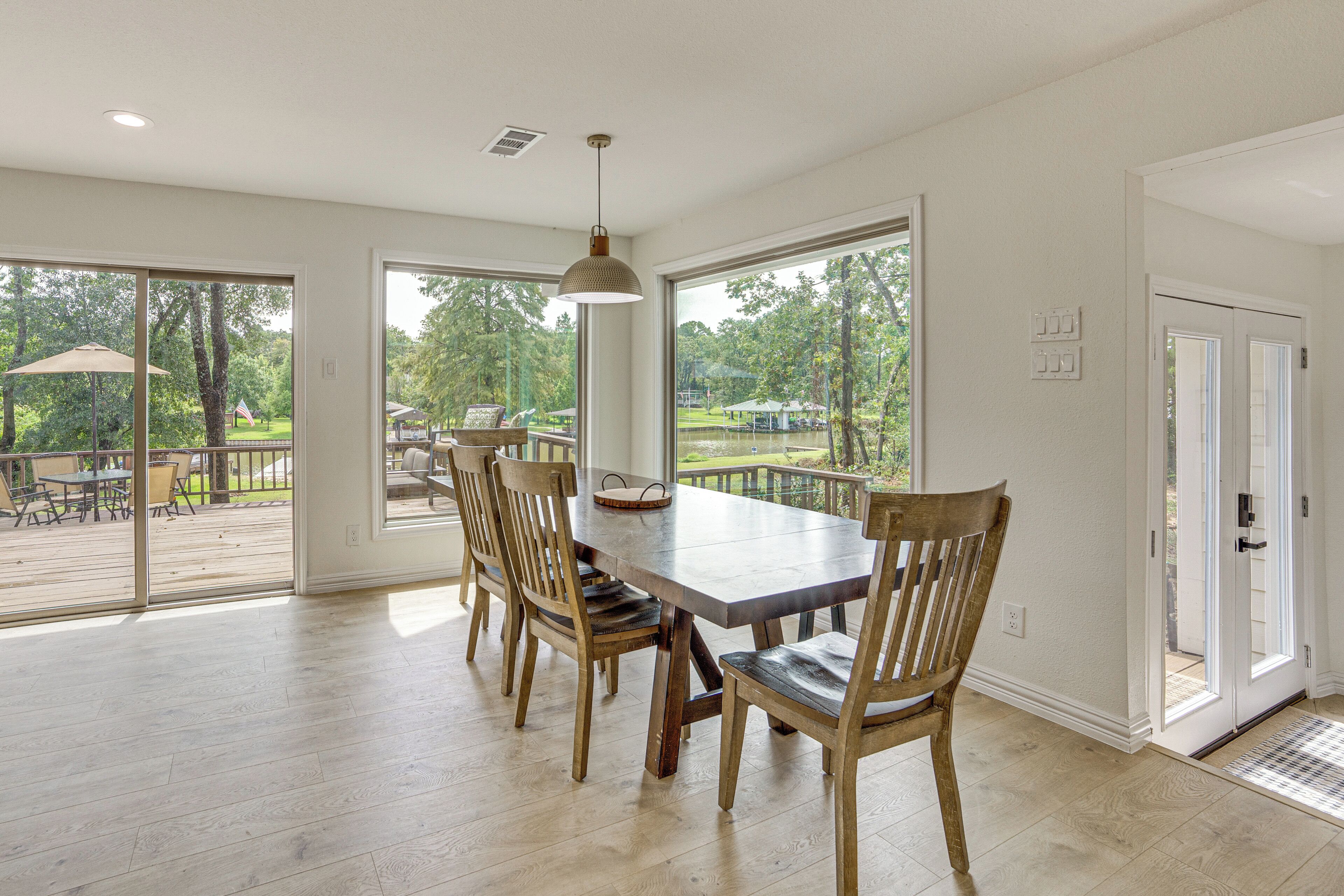 A dining area with a large table and chairs, large windows, and a view of a deck and outdoor area.