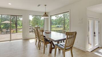 A dining area with a large table and chairs, large windows, and a view of a deck and outdoor area.