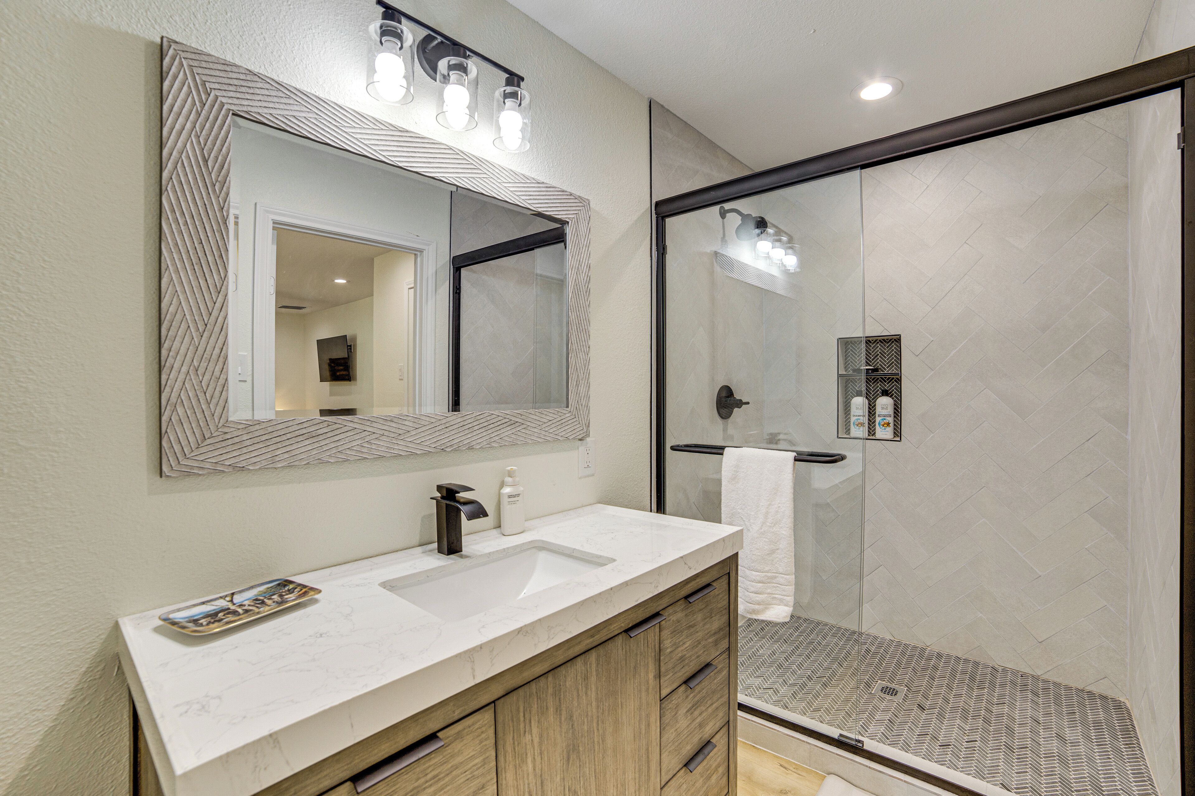 A bathroom with a large mirror, a sink, and a shower area.