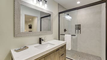 A bathroom with a large mirror, a sink, and a shower area.