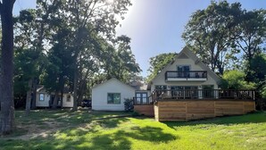 Propiedad residencial con una casa de dos pisos, una terraza de madera y un pequeño garaje adosado.