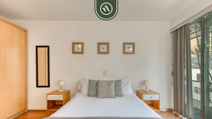 Ein modernes Schlafzimmer mit einem großen Bett, Nachttischen aus Holz und Blick ins Freie durch große Fenster.