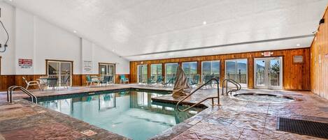 An indoor swimming pool with a stone floor, lounge chairs, and a hot tub.