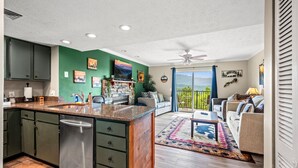 A modern kitchen with green cabinets, a stainless steel refrigerator, and a large island. There is a dining area with a sofa and a coffee table, and a balcony with a view of the mountains. - Mountain Views Indoor Pool Sauna Fireplace (Gatlinburg)