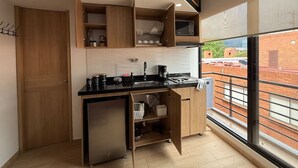 A modern kitchen with a built-in microwave, a coffee machine, and a small refrigerator. There is a large window providing a view of the cityscape.