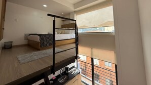 A high-rise apartment with a bunk bed, a kitchenette, and a large window offering a city view.