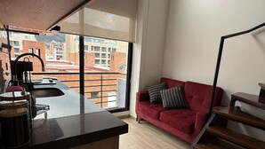 A modern kitchen with a large window, a red sofa, and a staircase.