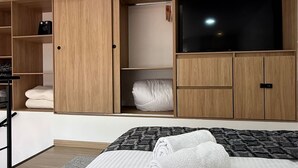 A modern bedroom with a large bed, a TV, and built-in wooden wardrobe with multiple compartments.