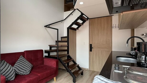 A modern living space with a red sofa, a wooden staircase, and a kitchen area.