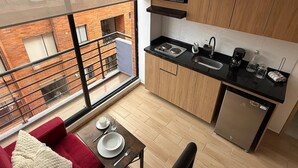 Cocina compacta con horno empotrado, microondas y lavavajillas, zona de comedor con mesa para dos y balcón con vistas a la ciudad.