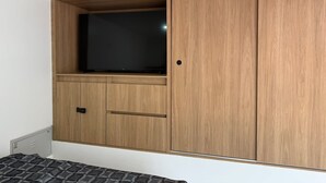 Un dormitorio con una cama, un armario con televisor y un mueble pequeño.