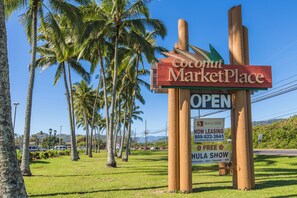 Placa do Coconut MarketPlace com aviso de 'ABERTO', anúncio de 'ALUGUEL DISPONÍVEL' e propaganda de 'SHOW DE HULA GRÁTIS'.