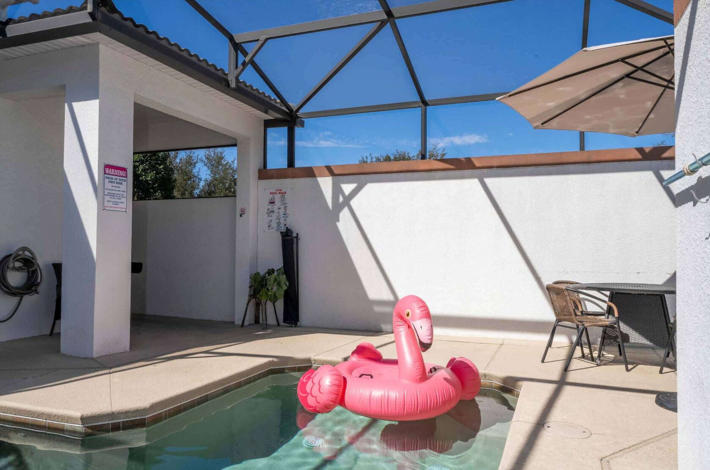 Una piscina con un giubotto a forma di fenicottero rosa, una zona patio coperta e mobili da esterno.