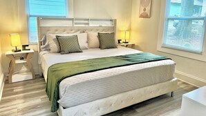 Un dormitorio ordenado con una cama grande, dos mesitas de noche con lámparas y una ventana con persianas.