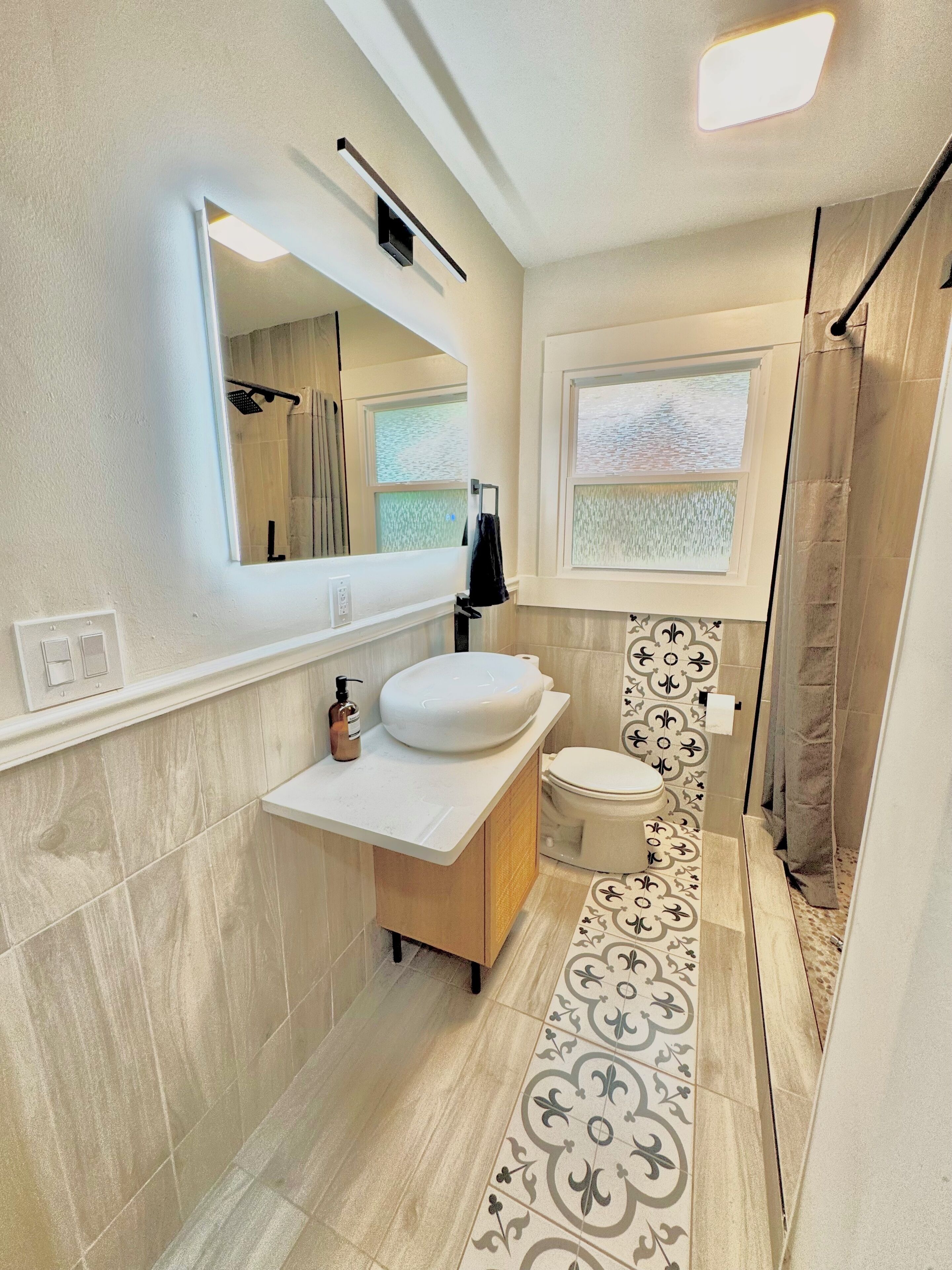 A modern bathroom with a large mirror, a white sink, a toilet, and a shower area.