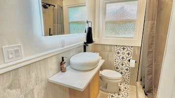 A modern bathroom with a large mirror, a white sink, a toilet, and a shower area.