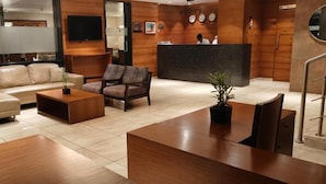 A modern hotel lobby with a reception desk, leather sofas, wooden coffee table, and a potted plant. - JK PARK RESIDENCY PERAMBRA (Perambra)