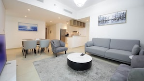 A modern living room with a grey sofa, a round coffee table, and a dining area with chairs and a table. - Silk Valley - Luxury 2B near Dubai Mall (Dubai)