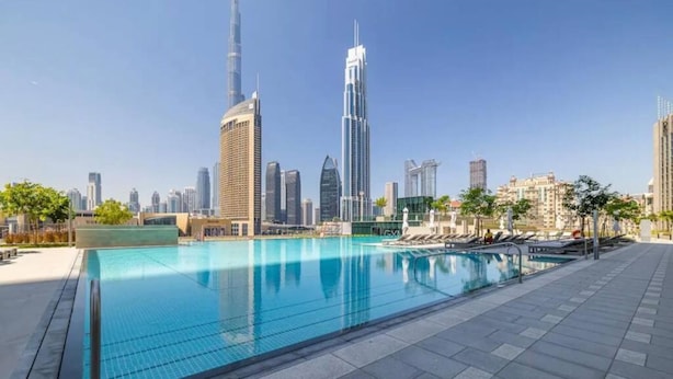 A swimming pool with lounge chairs and a city skyline in the background. - Silk Valley - Luxury 2B near Dubai Mall (Dubai)