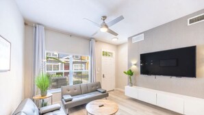 Un salón moderno con un sofá gris, una mesa de centro redonda y un televisor de pantalla plana en la pared.