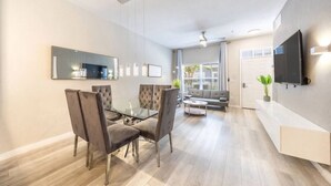 Una sala de estar moderna con una mesa de comedor de vidrio, sillas acolchadas, un sofá, un televisor y un ventilador de techo.