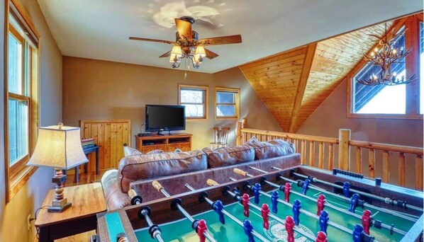 A cozy room with a foosball table, a television, a sofa, and a ceiling fan.