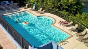 Piscina rectangular con una sección curva, rodeada de sillas de descanso y una valla.