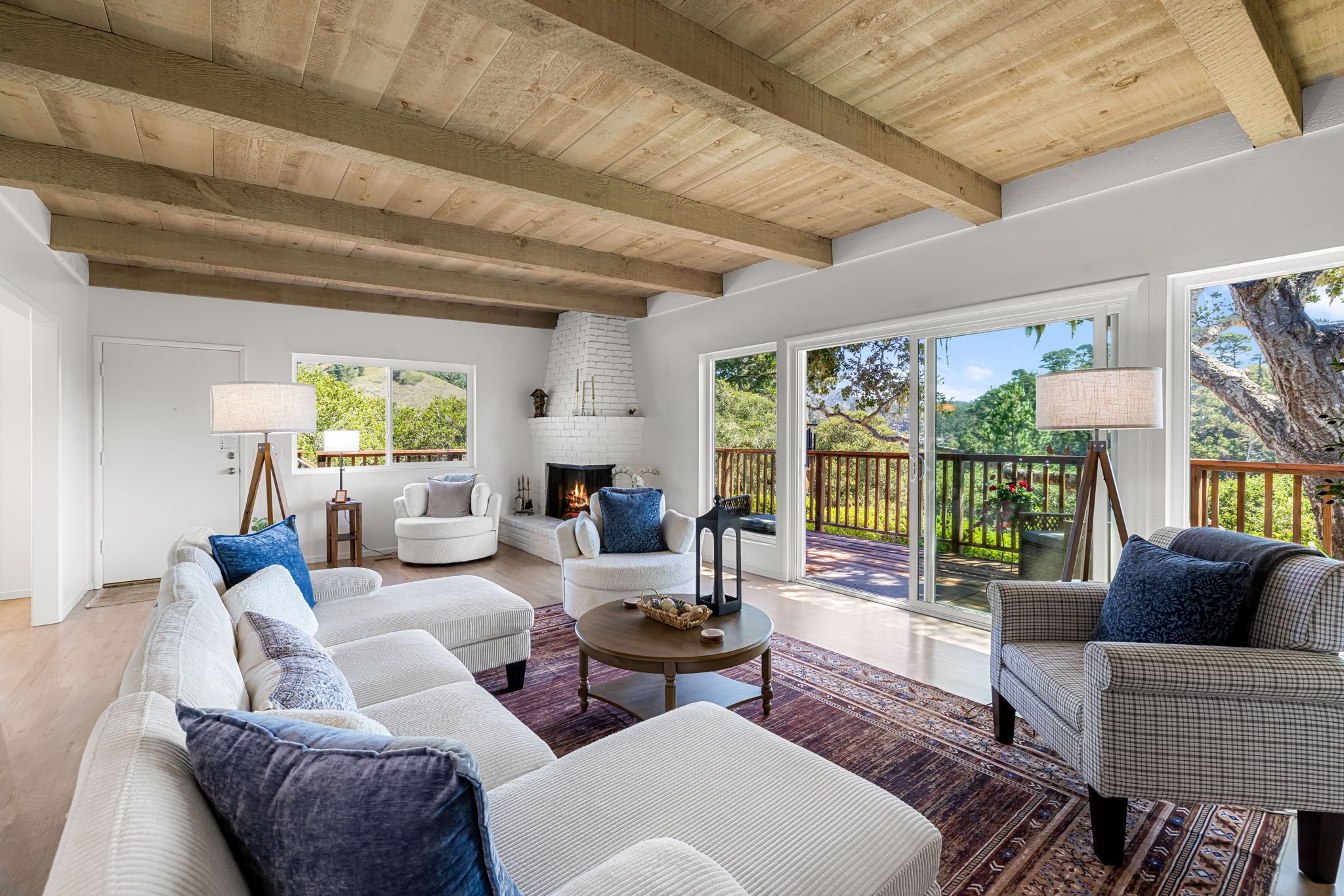 A spacious living room with a high ceiling, white walls, and large windows offering a view of the outdoors.