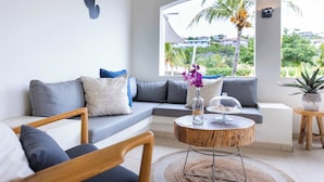 Ein modernes Wohnzimmer mit einer Couch, einem runden Couchtisch und Blick auf Palmen.