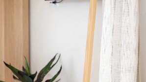 Ein Zimmer mit an der Wand montiertem Fernseher, einem hölzernen Malkasten und einer Pflanze auf einem kleinen Hocker.