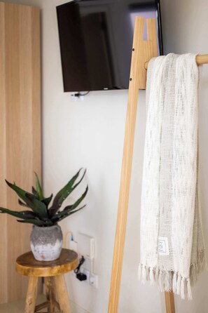 A room with a wooden floor, a potted plant, a television mounted on the wall, and a wooden easel with a white cloth draped over it.