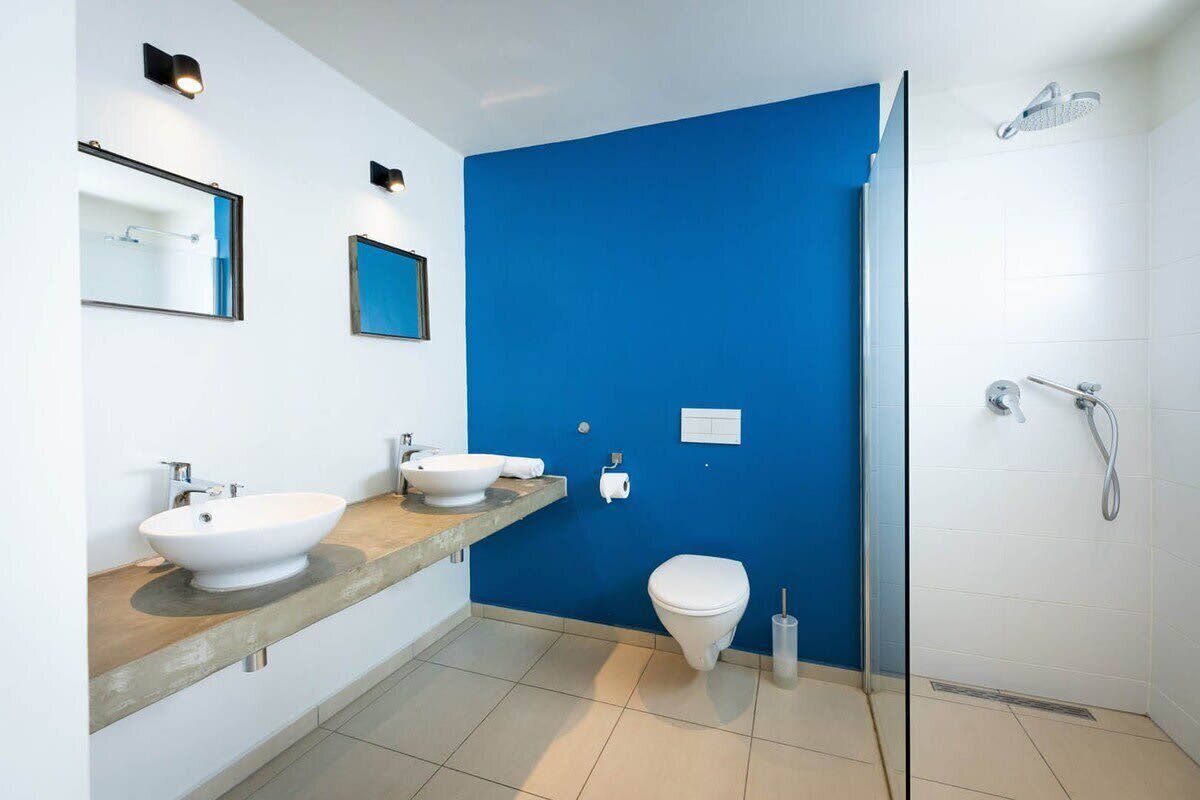 Een moderne badkamer met een grote spiegel, twee wastafels, een toilet en een douchecabine met glazen wanden.