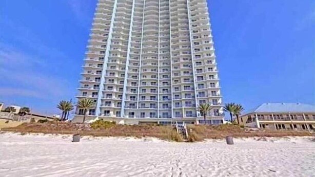 A tall, multi-story hotel with balconies, located near a sandy beach.