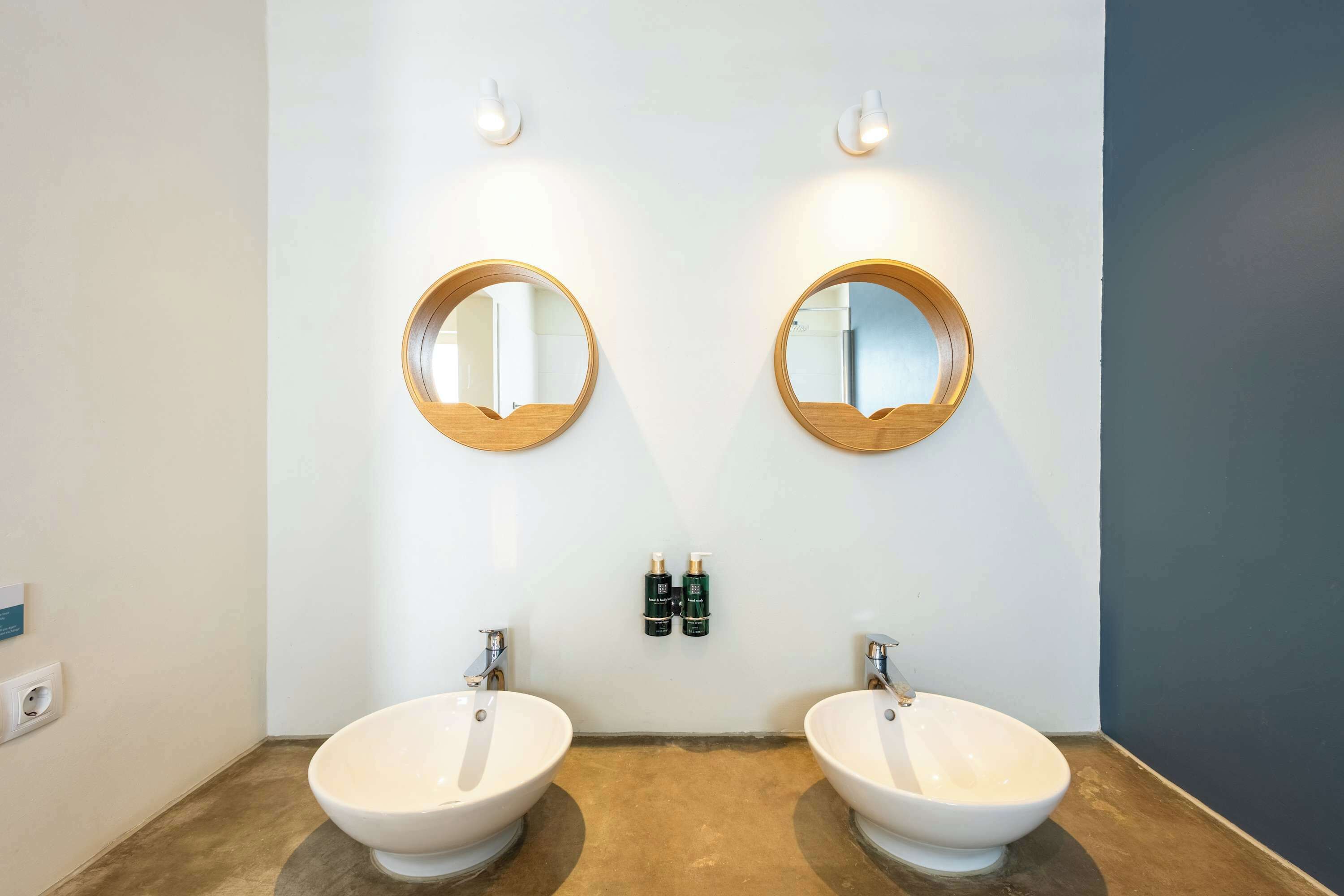 A bathroom with two sinks, two round mirrors, and two wall-mounted light fixtures.