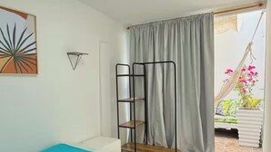 Un dormitorio con cama, ventana con cortinas, un sillón colgante y vistas a un balcón con plantas.